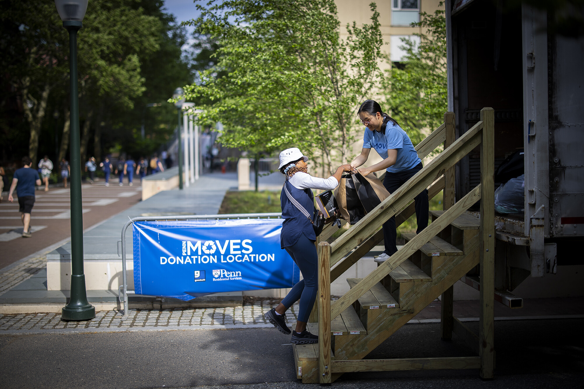 Person gives bag to another person staffing donation truck with PennMOVES "Donation Location" sign in background