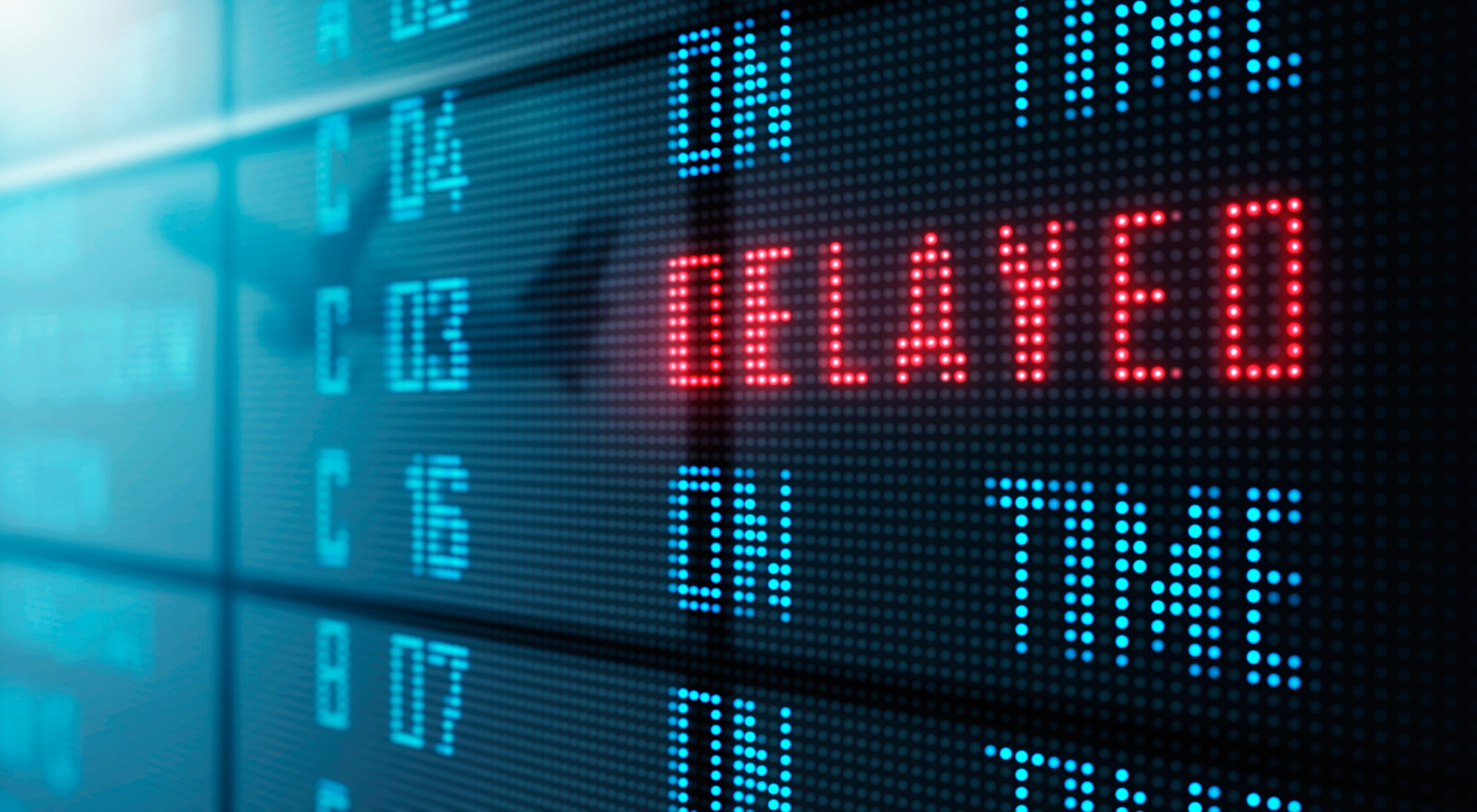"Digital display showing the word 'DELAYED' in red alongside other information in blue on an airport board.