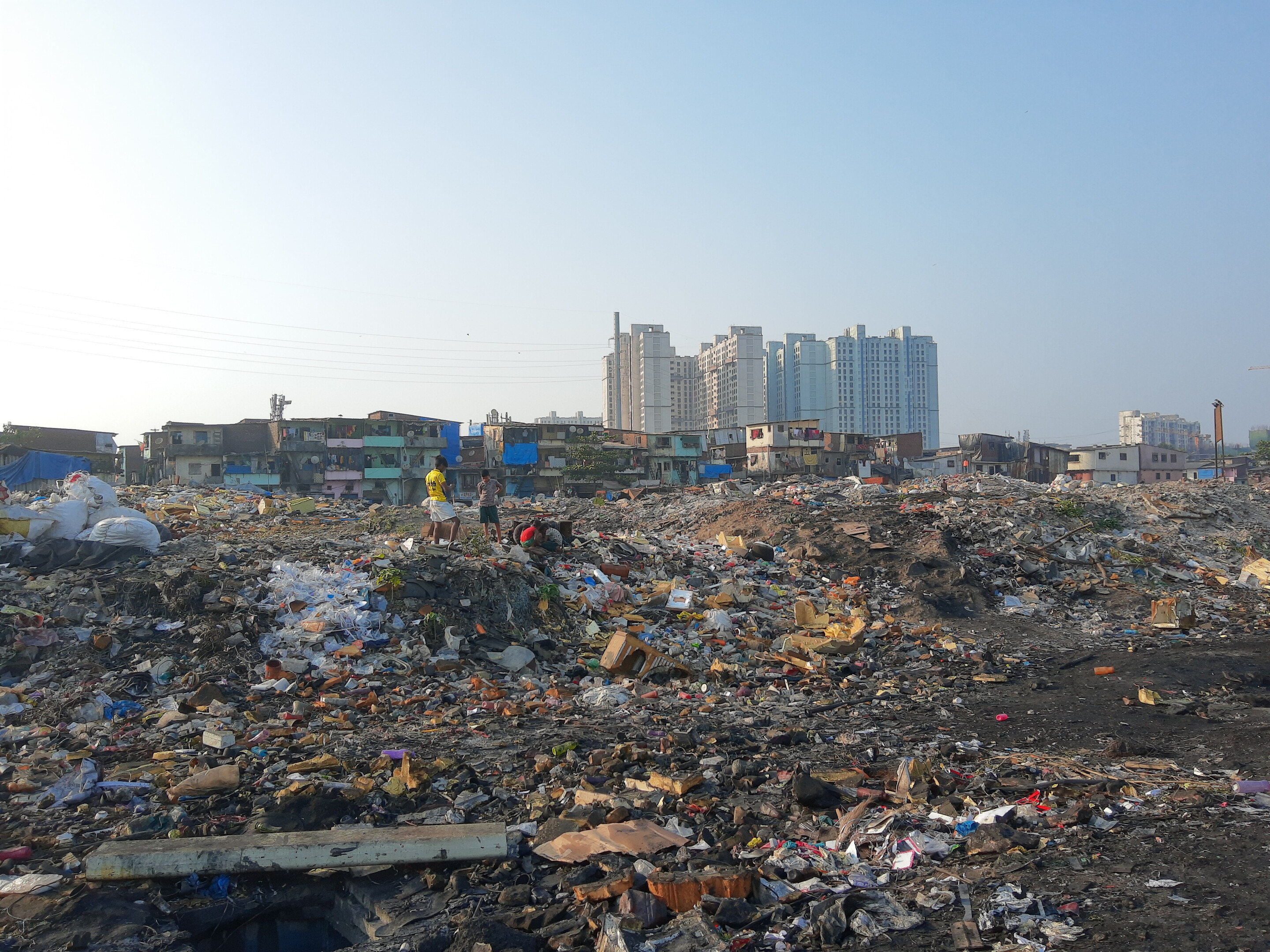 An image of people picking through a dump with a handful of skyscrapers along the horizon
