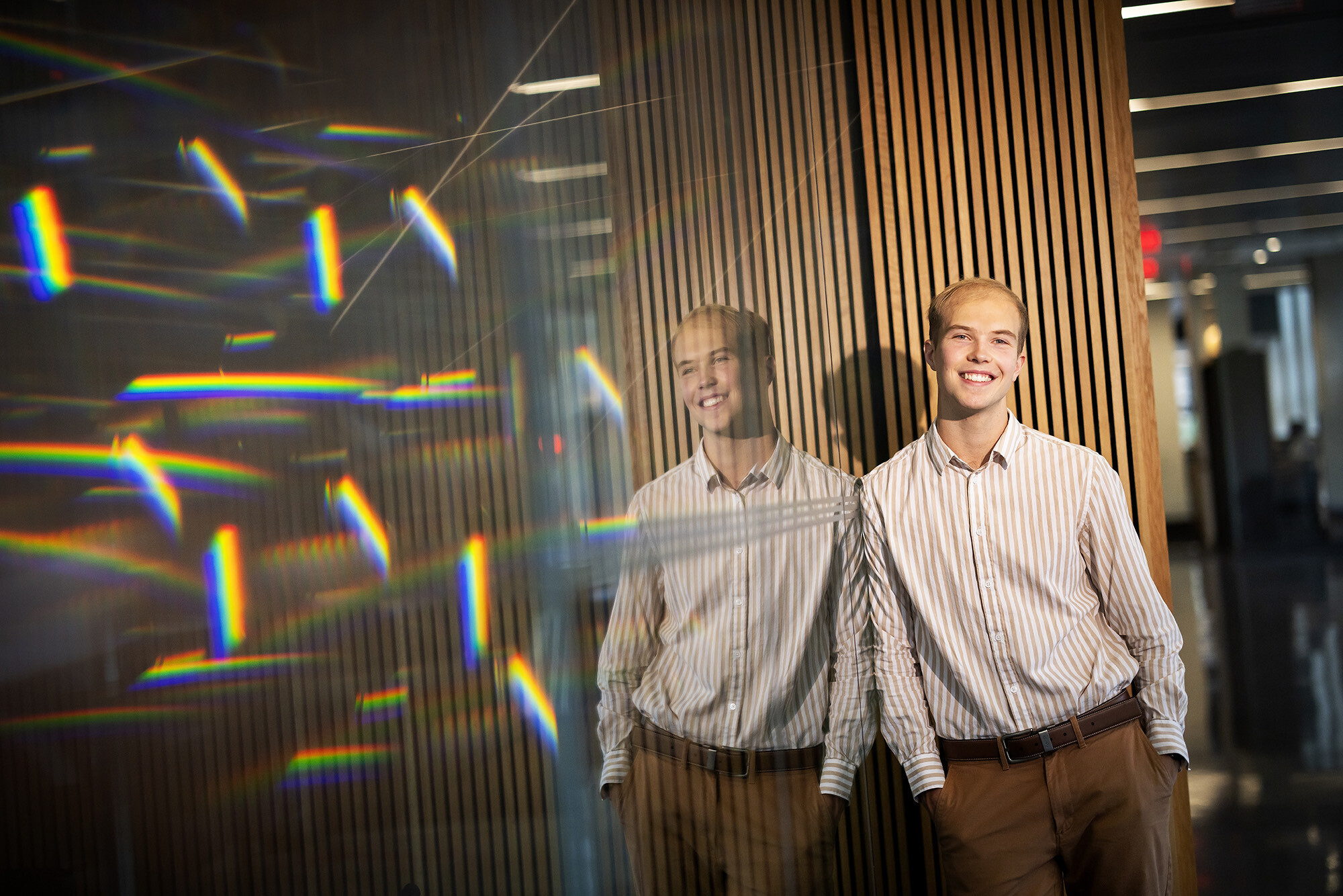 Silas Ruth poses near a glass wall with reflective rainbows.