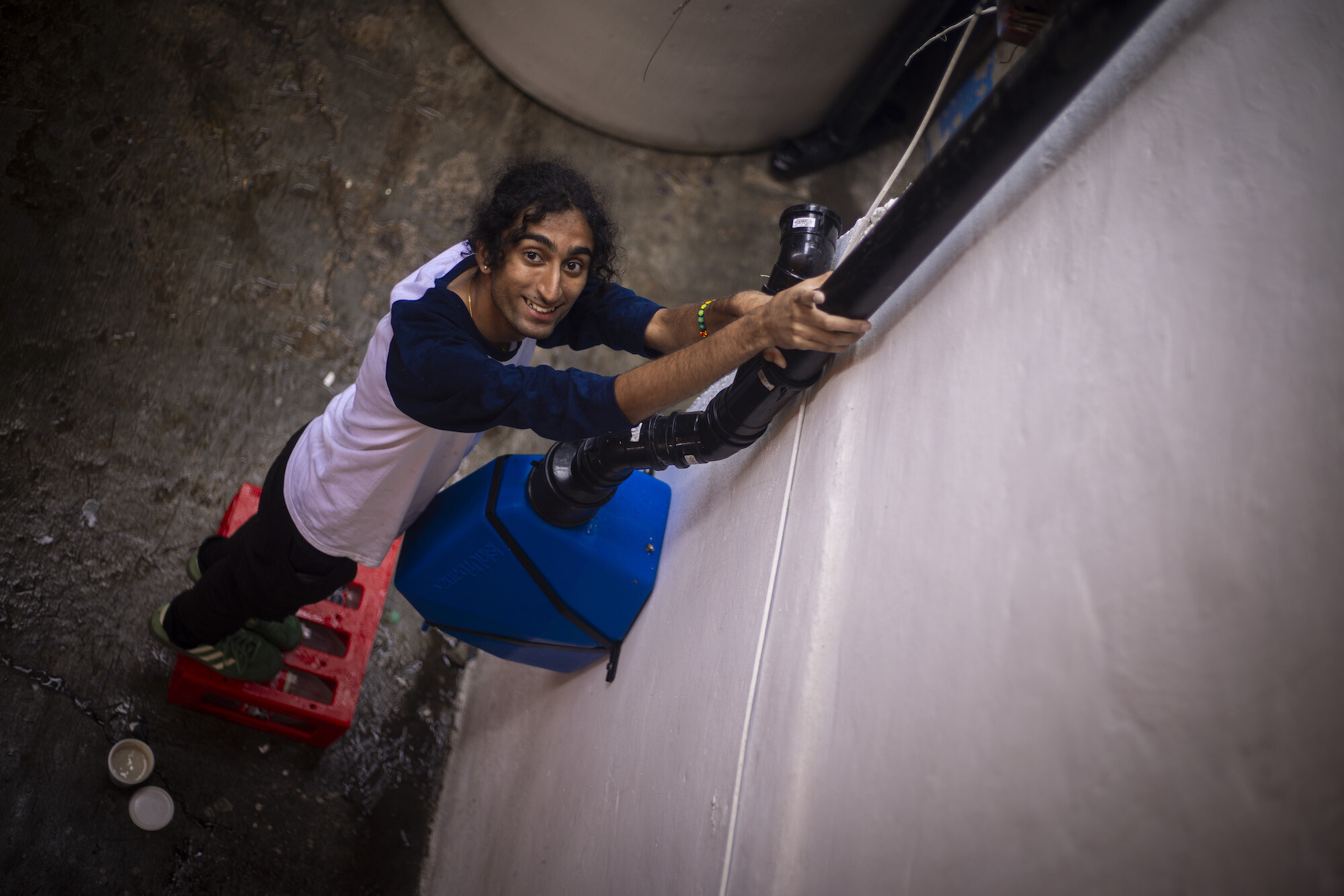 Krishna Chandrasekhara stands on a milk crate, holding plastic water piping for a rooftop water harvesting system in Mexico.