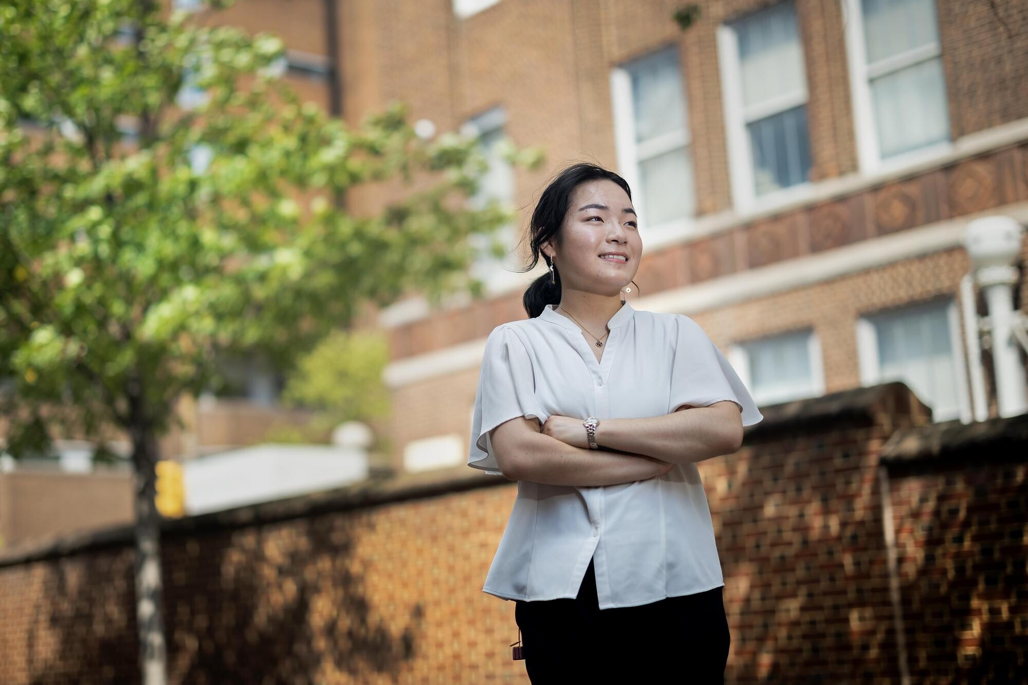Eri Maeda standing outdoors with arms crossed and looking to the side with a smile.