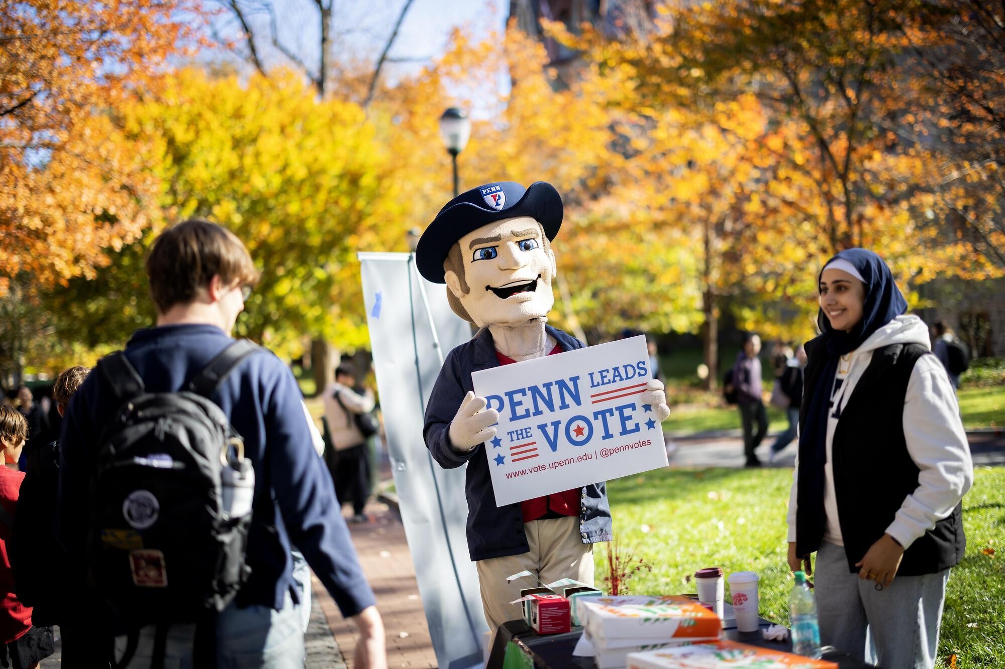 The Penn Quaker mascot holding a Penn Leads the Vote sign on Locust Walk.