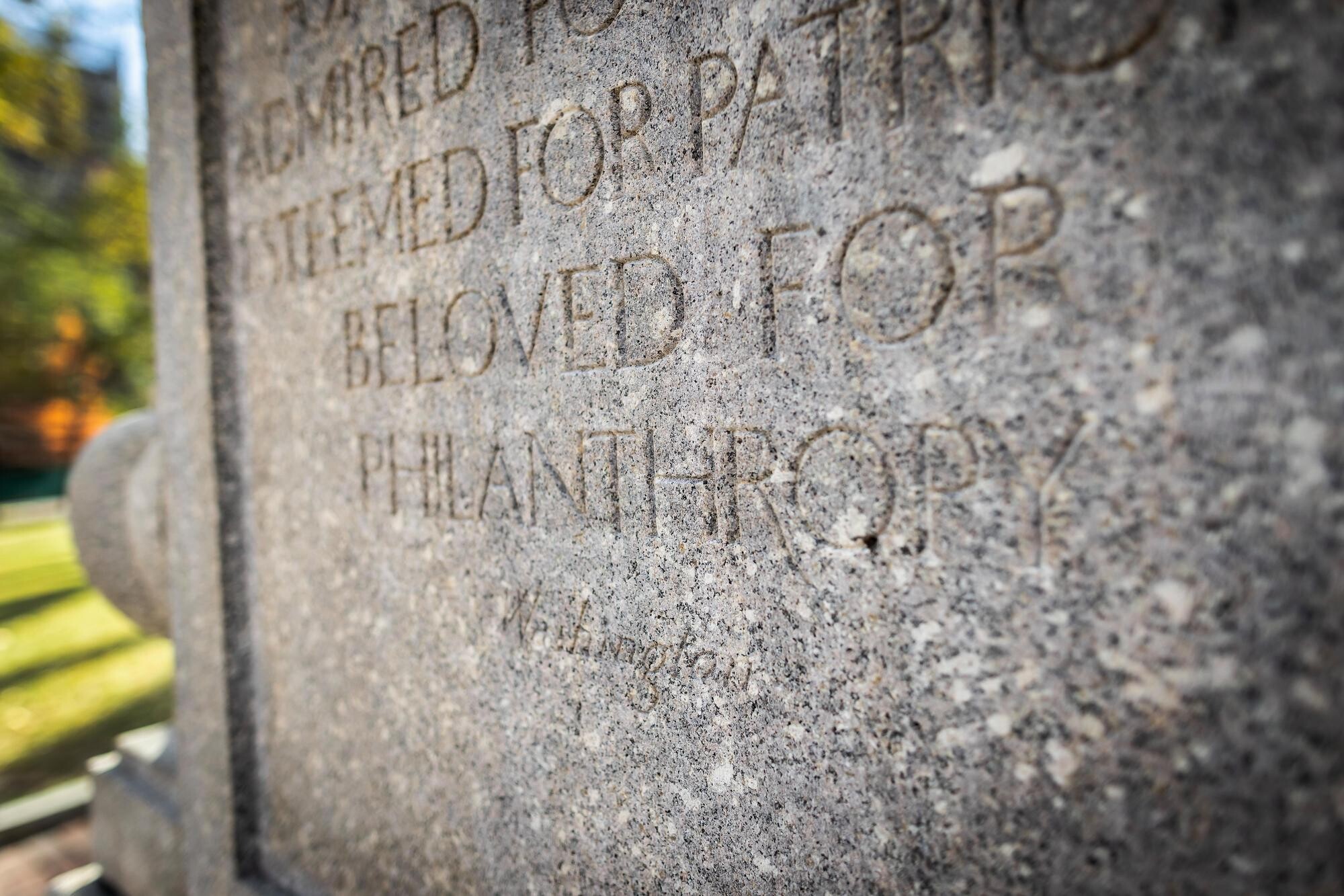 A stone marker with writing, among the words are “BELOVED FOR PHILANTHROPY.”