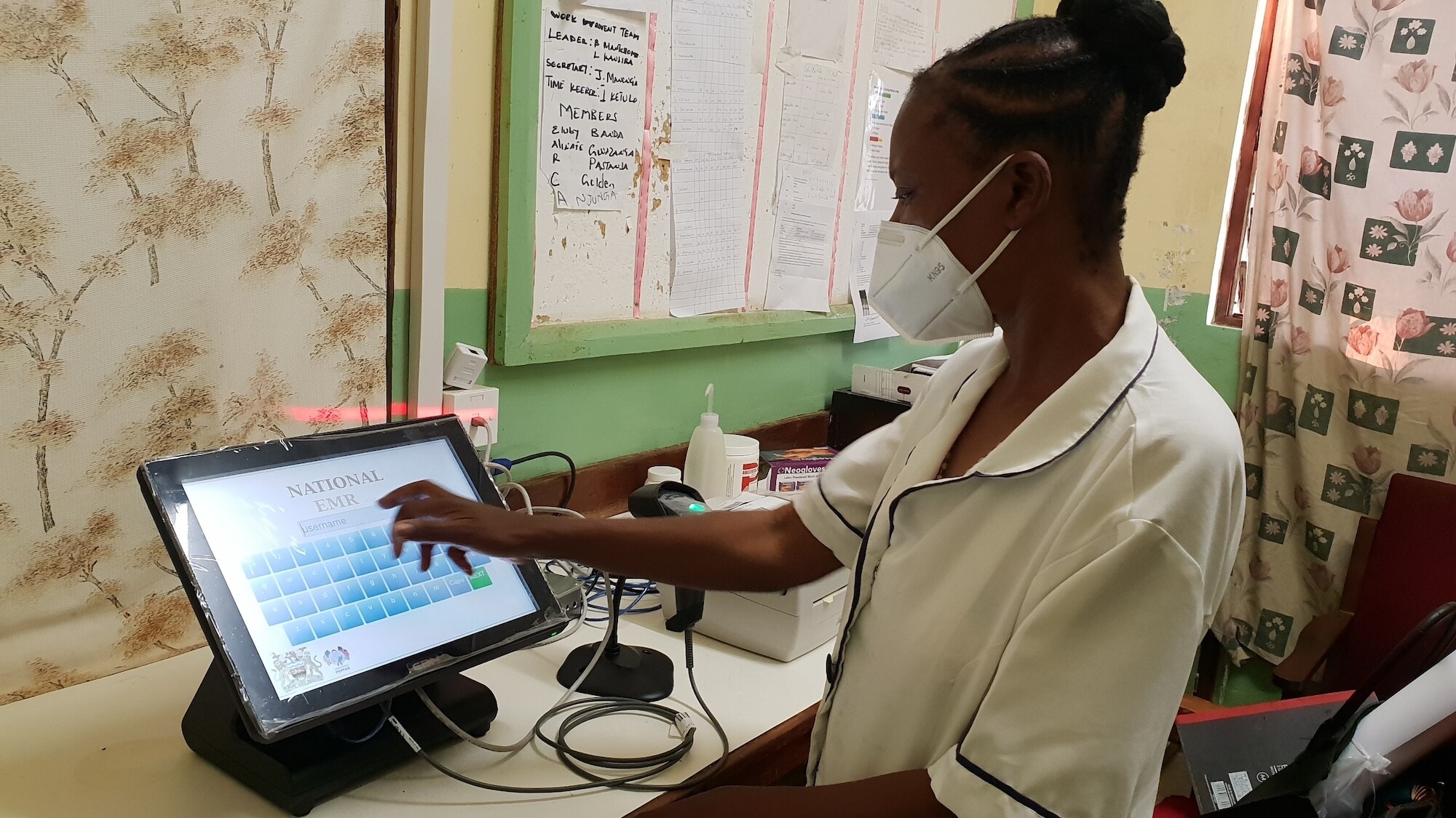 Health care worker in mask stands at tablet with electronic medical record system.