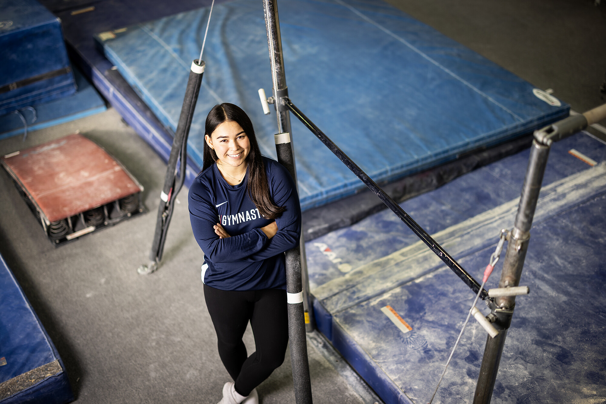 Carly Oniki leans against a gymnastics pole in the training center.