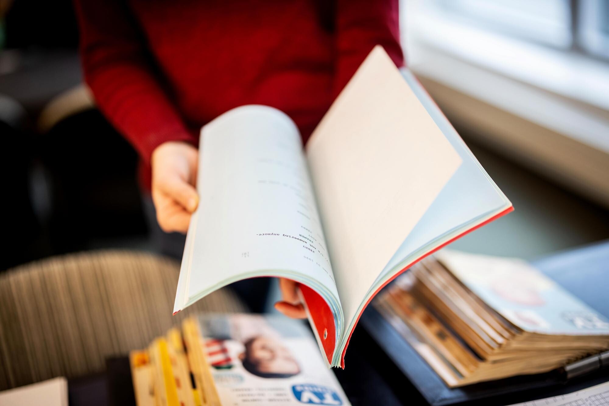 A person flipping through a book with old TV Guides on the table below them.