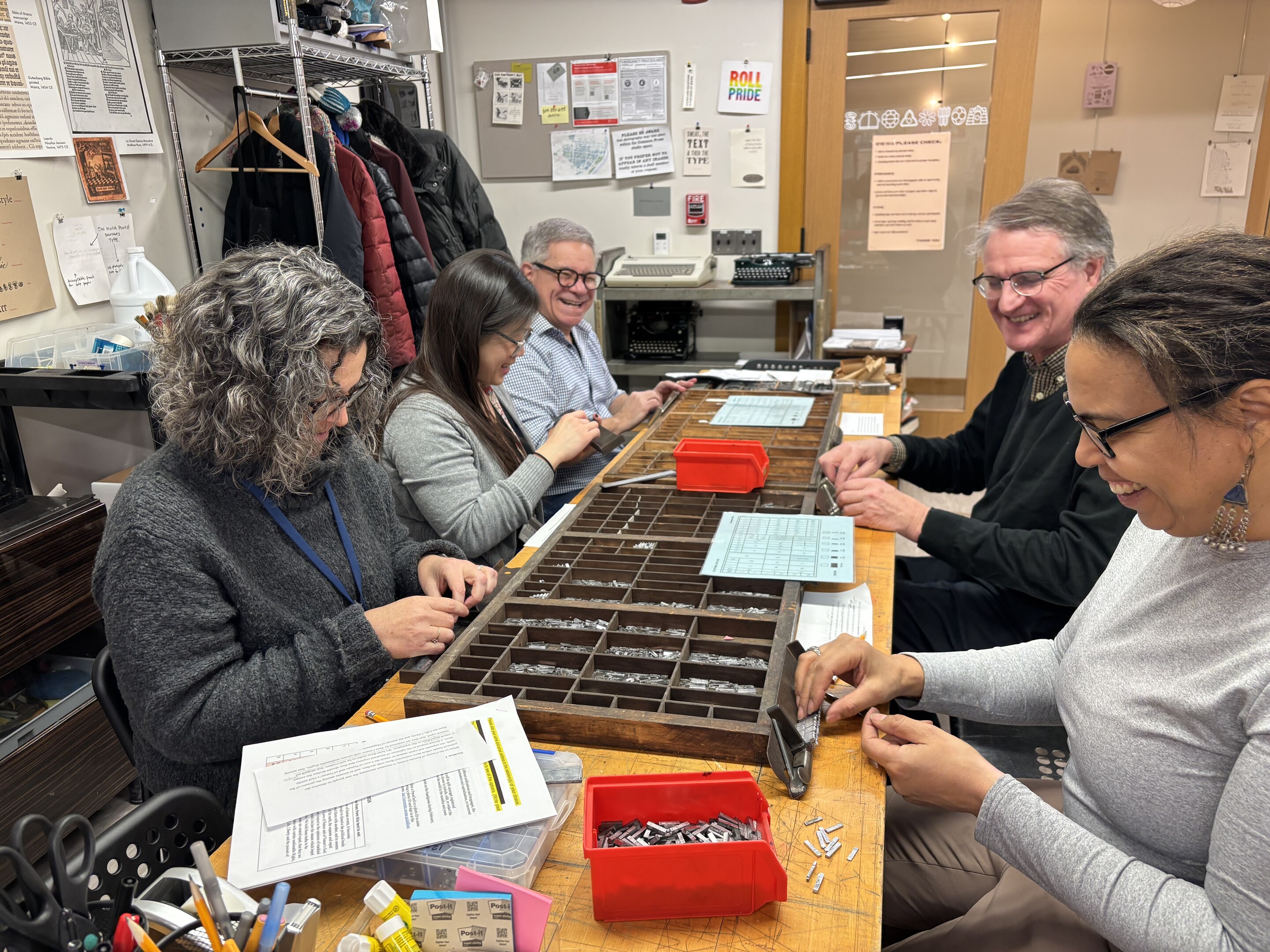 Five workers seated at a table at Common Press selecting small letters for letterpress.