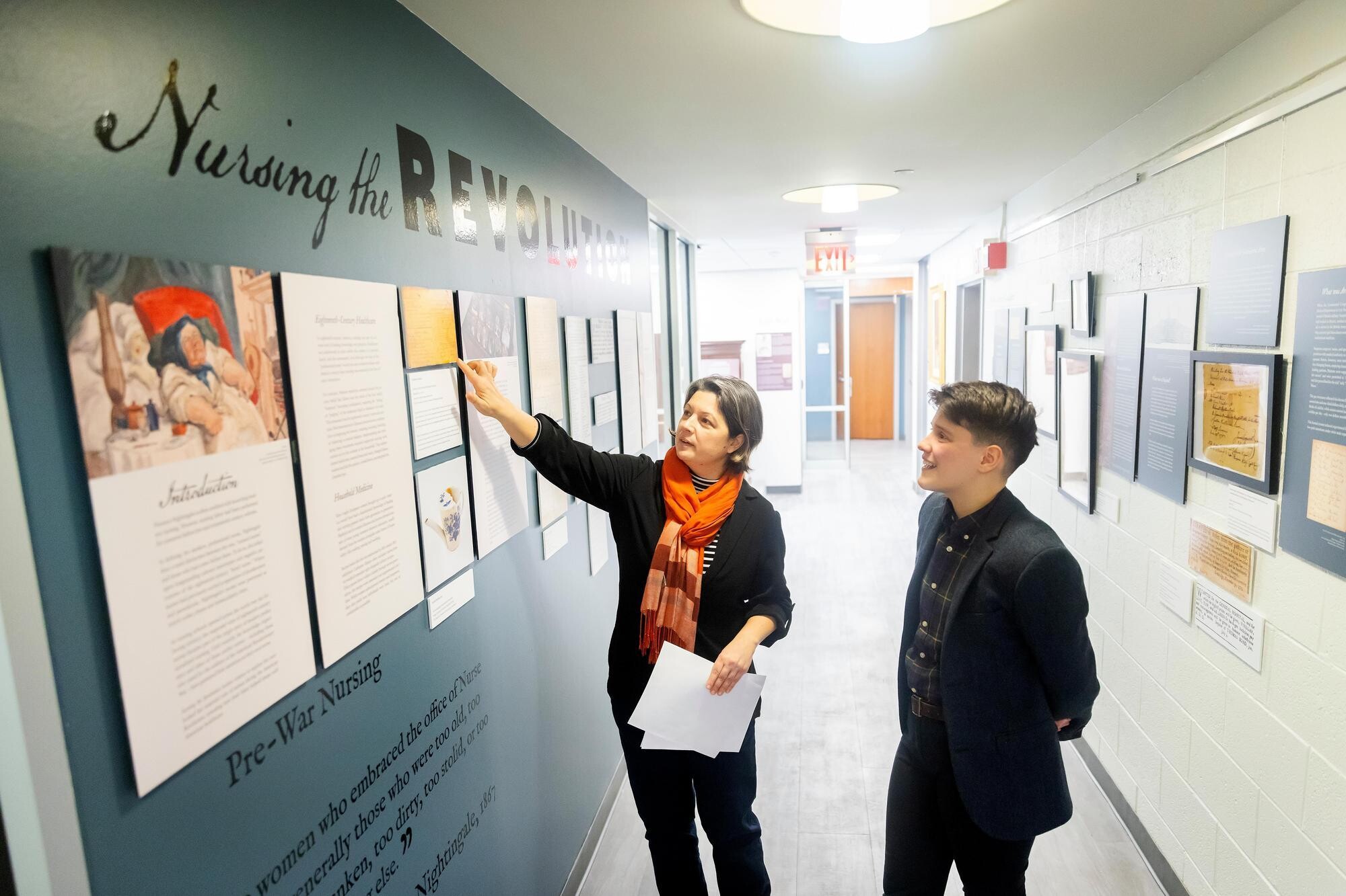 Meg Roberts and Jessica Martucci looking at the Nursing the Revolution exhibition wall.