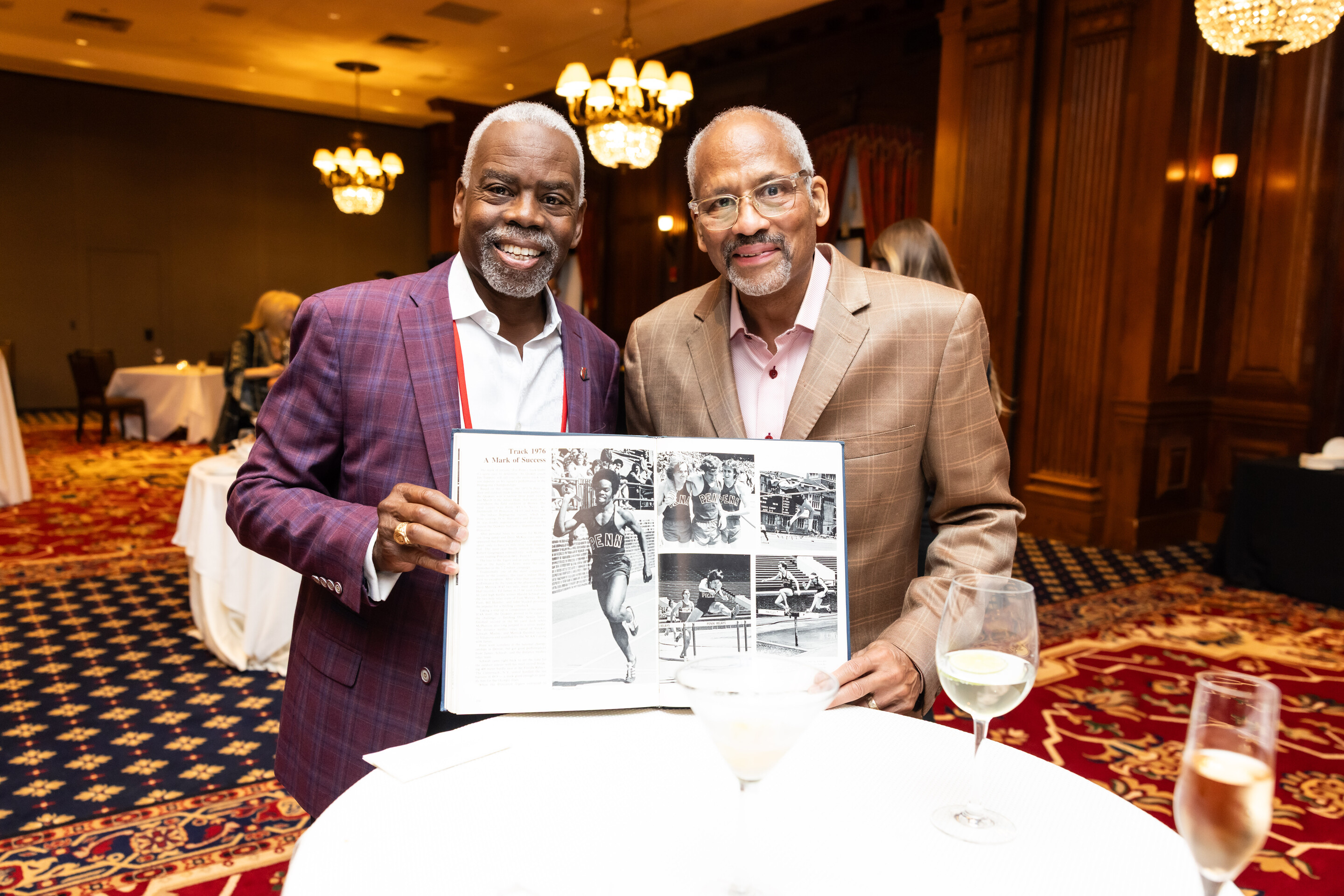 two penn alums holding a black and white yearbook with track runners.