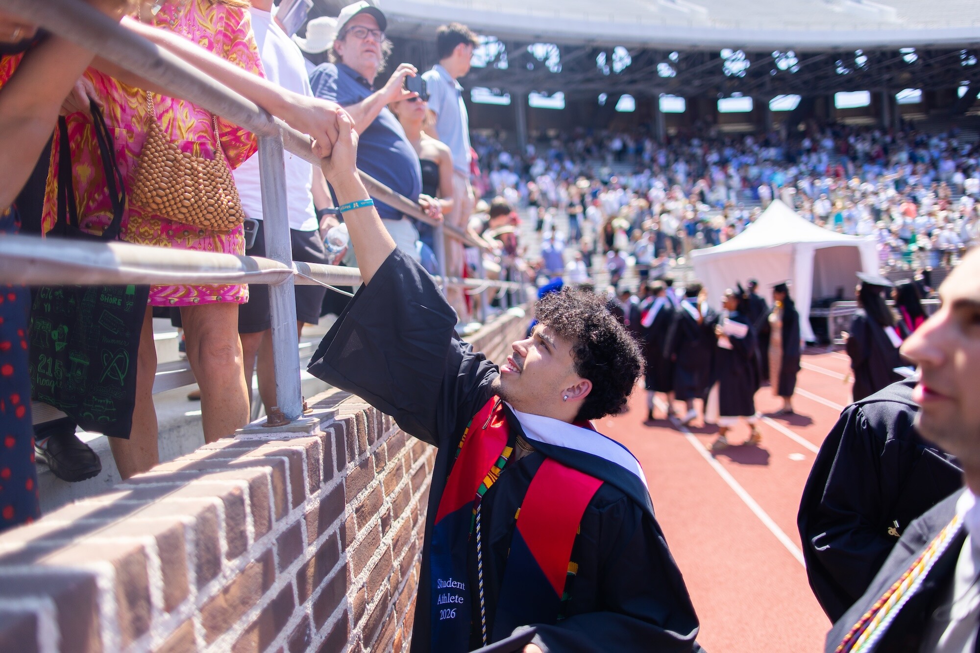 A graduate taking the hand of a loved one in the stands during Commencement.