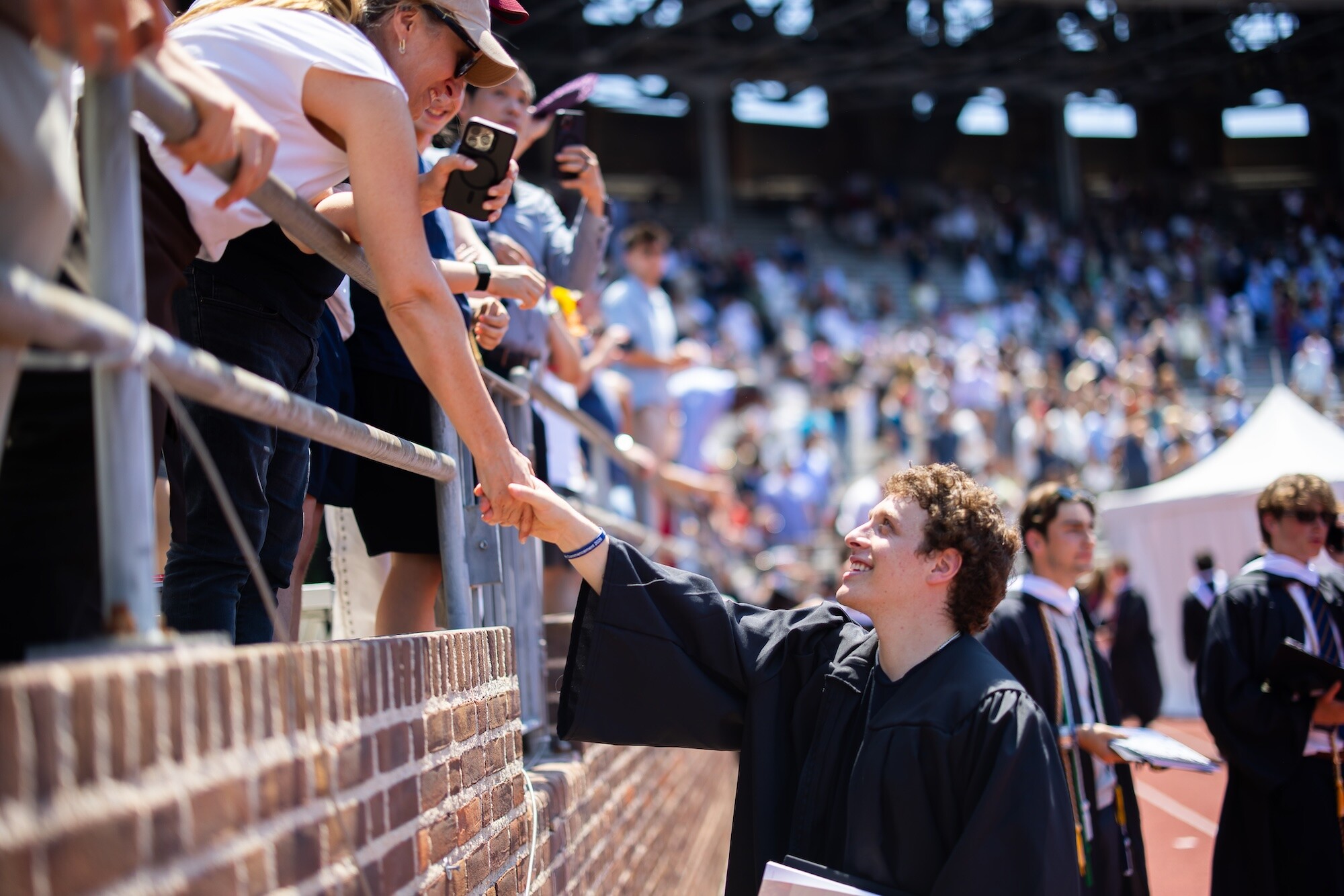 A graduate holding the hand of a loved one in the stands at Penn’s commencement.