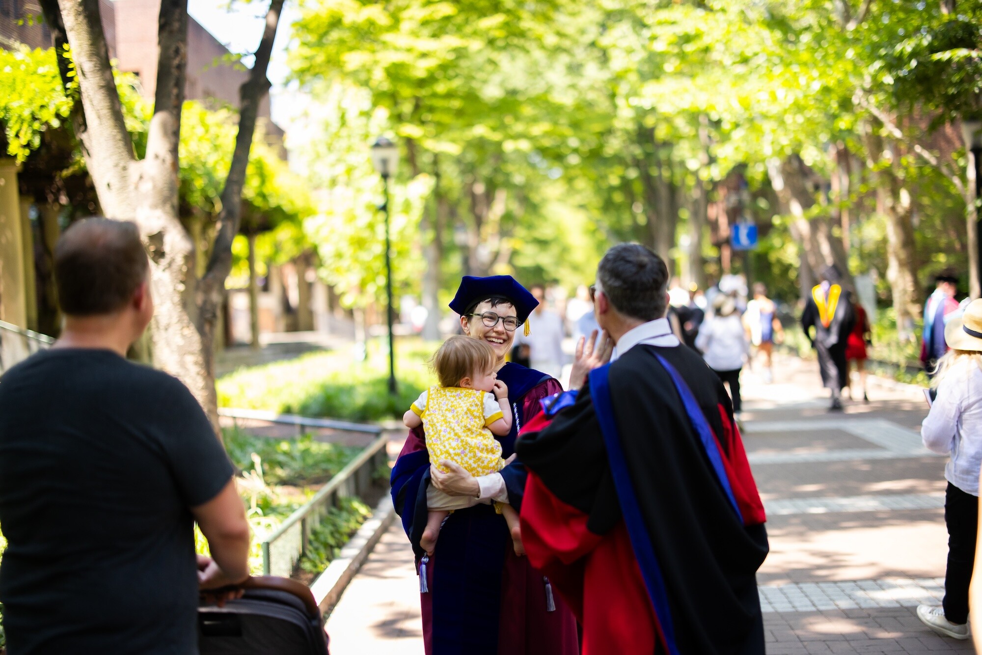 A graduate holding a baby on Locust Walk after commencement.