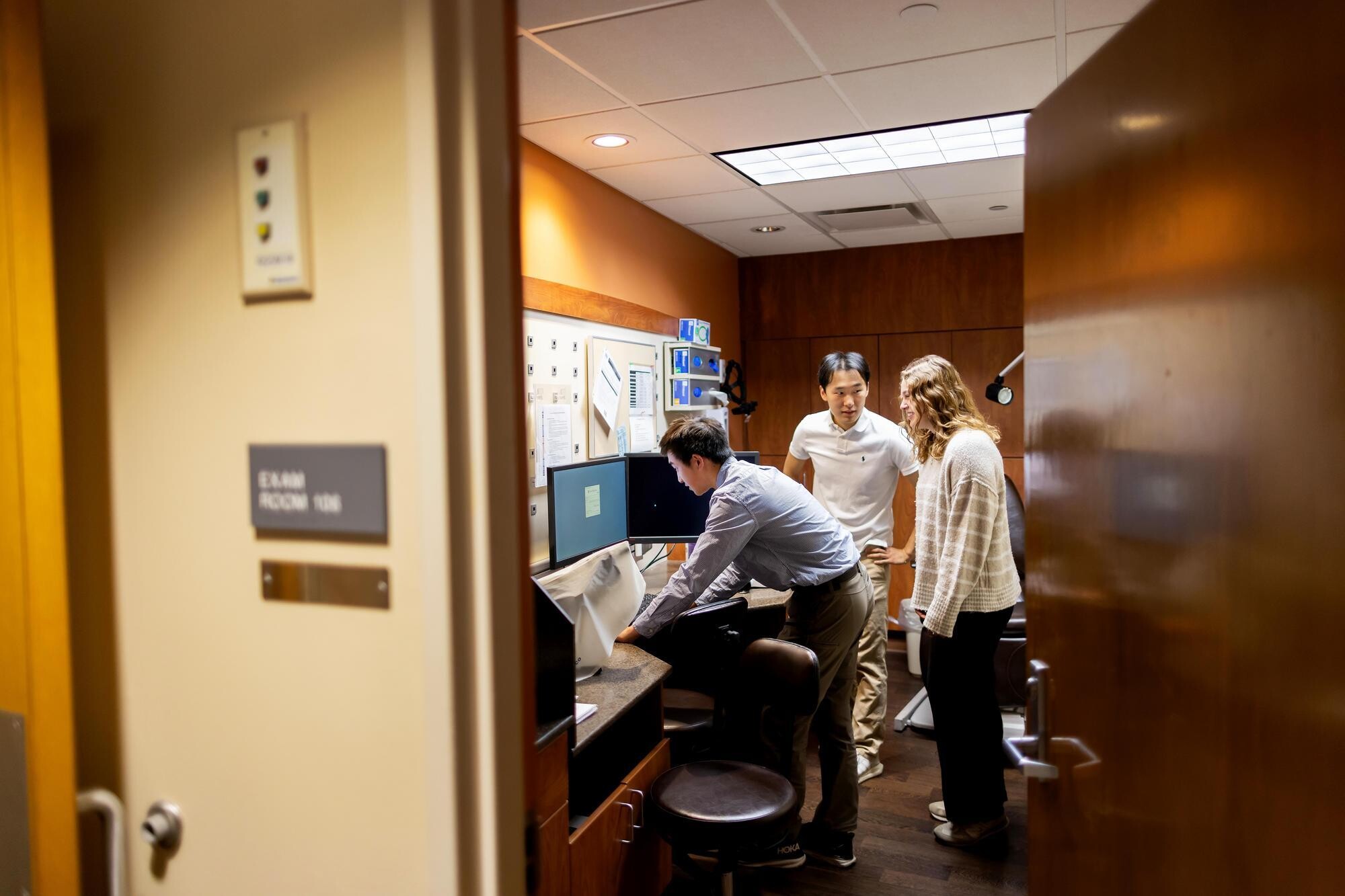From left to right: Eric Lee, Justin Wang, and Janine Haros in a clinical room at the Scheie Eye Institute, looking at a computer and speaking with each other