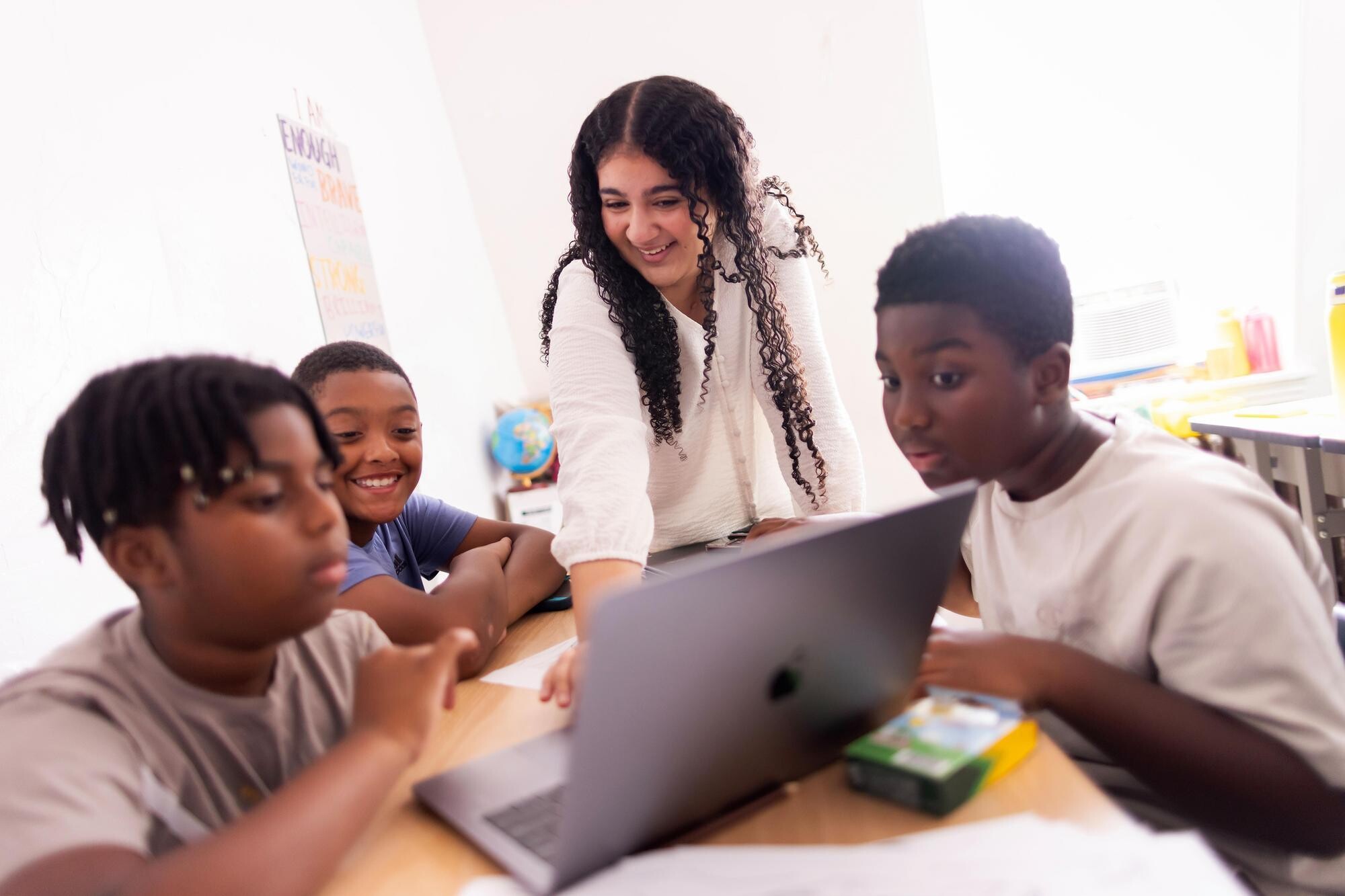 Sarah Attia stands at laptop with three kids.