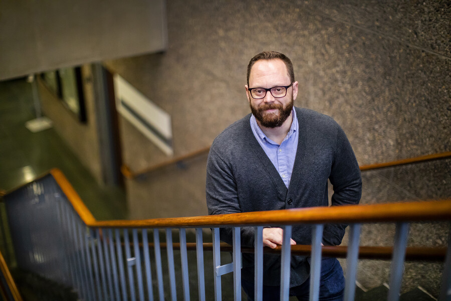 Jesse Raines poses on a staircase, looking up at the camera and smiling.
