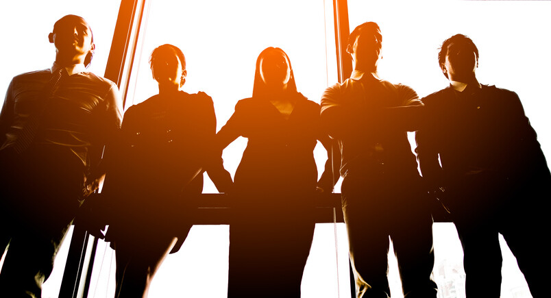 six people standing by a window backlit by the sun
