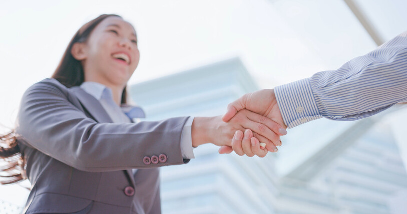 closeup of a young woman in a suit shaking hands with another person off-camera