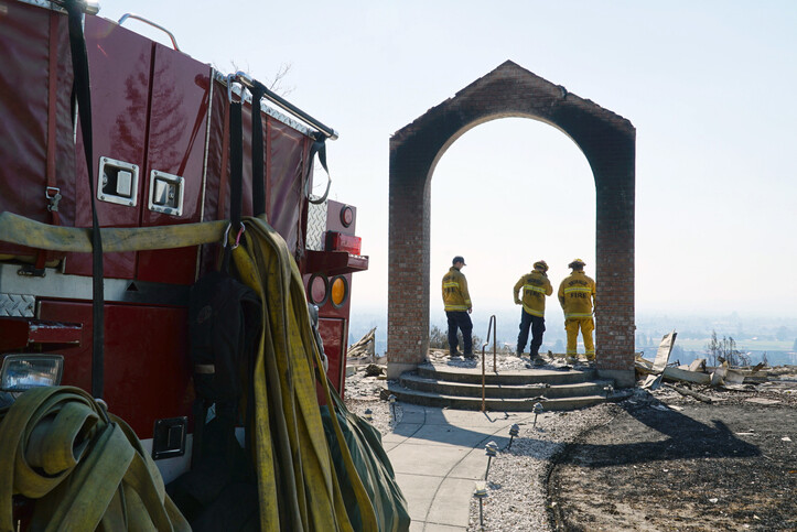 firefighters in remaining archway of a destroyed building with side of firetruck in foreground