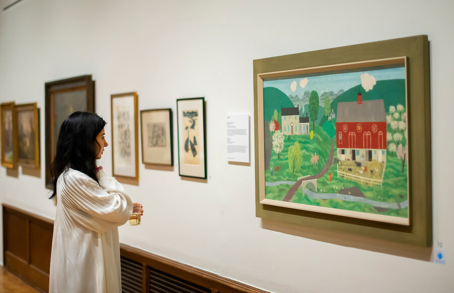 woman in profile looking at folk art painting of a red barn and white farmhouse