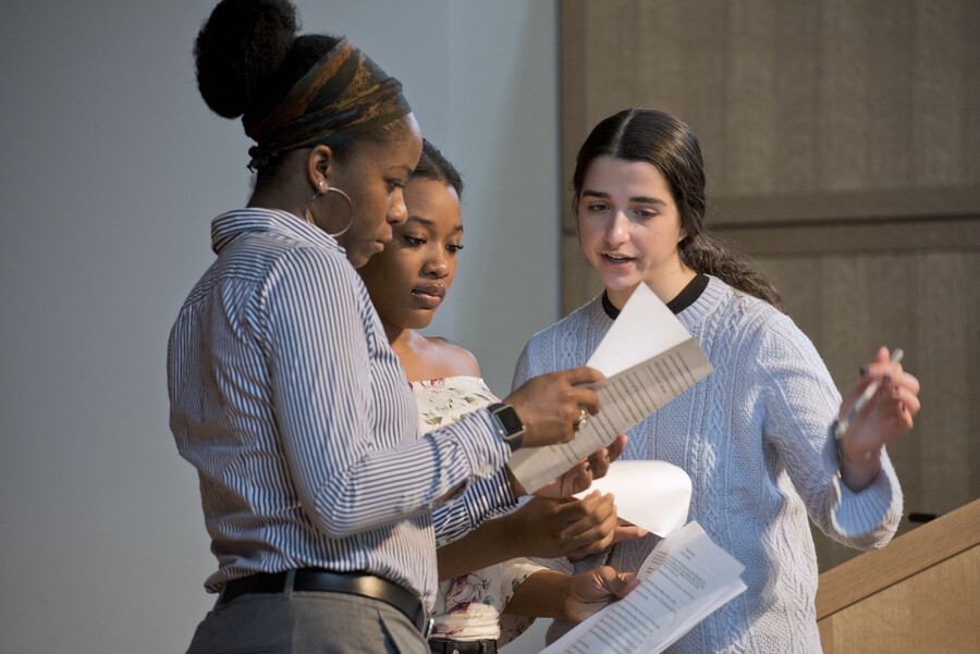 three women standing in a circle reading a script and discusssing