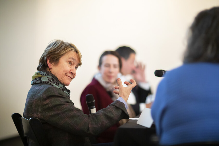 Speaker at conference, seated, gestures to indicate a point.