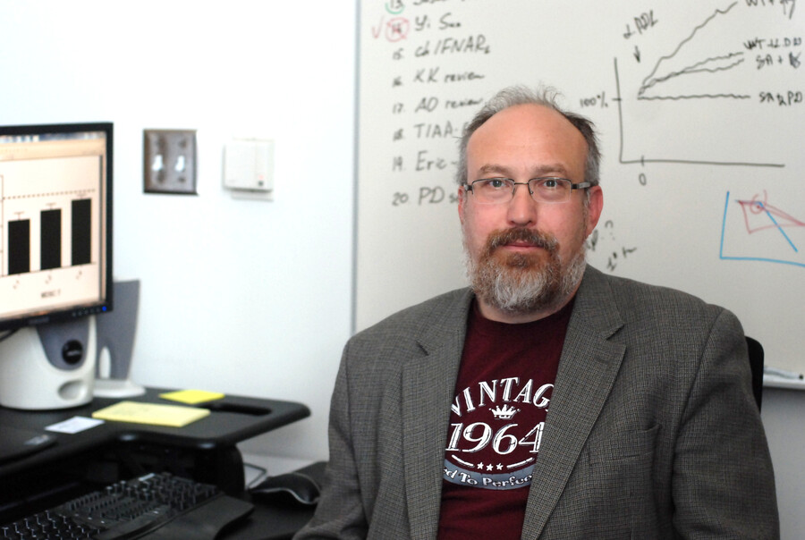 Professor in office with scientific notations on a computer and a whiteboard behind him.