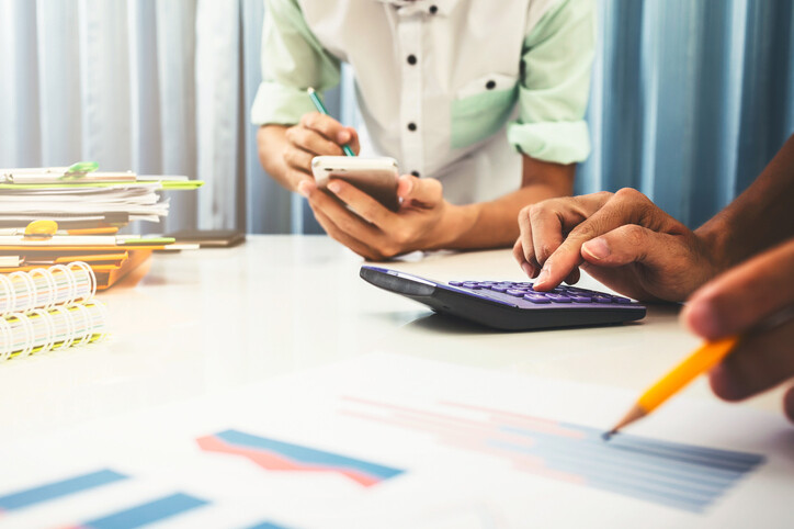 two people at a desk with calculators, papers, pens and pencils