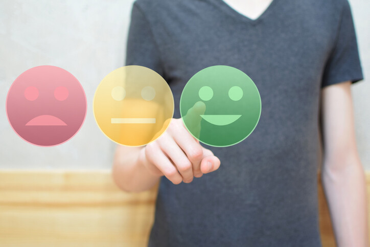 Person pressing one of three large digital buttons with a happy, neutral, and frown face.