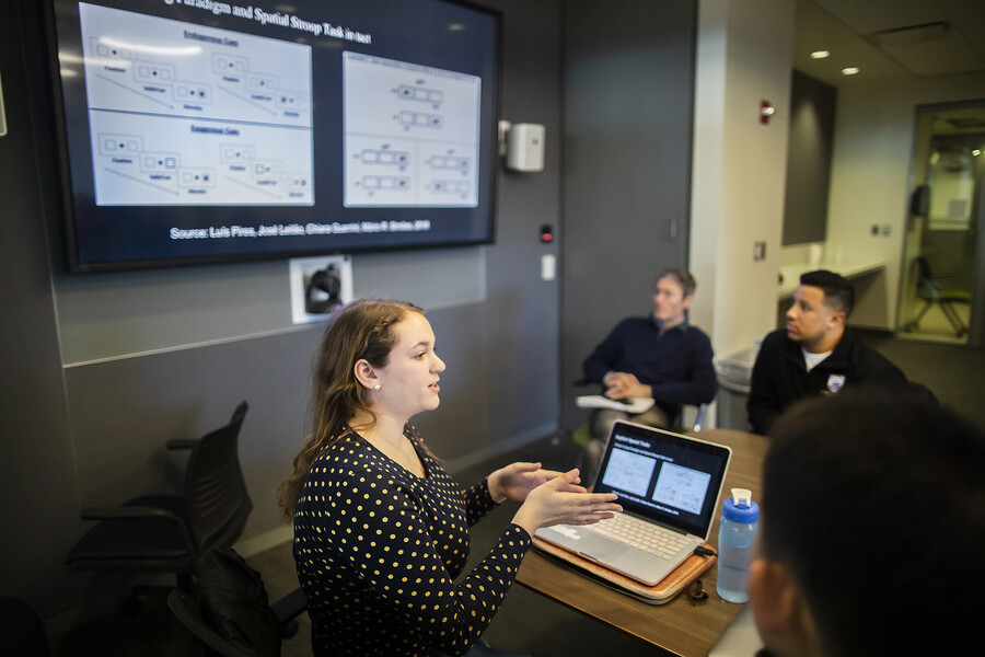 A girl in a polka dot shirt in front of a computer gesturing with her hands. 