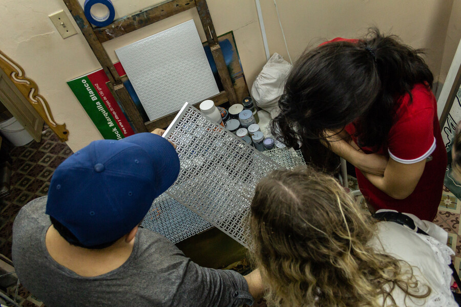 Three people looking at metal mesh and paints. 