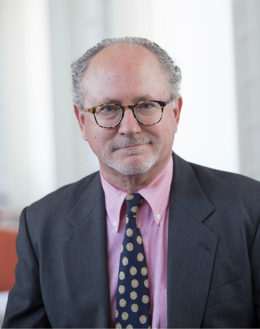 A man in glasses with a pink shirt, blue tie and blazer. 