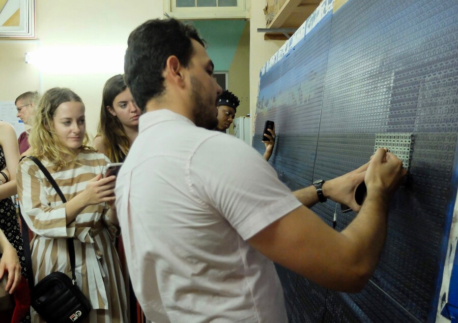Artist holds metal mesh up to painting while students watch. 