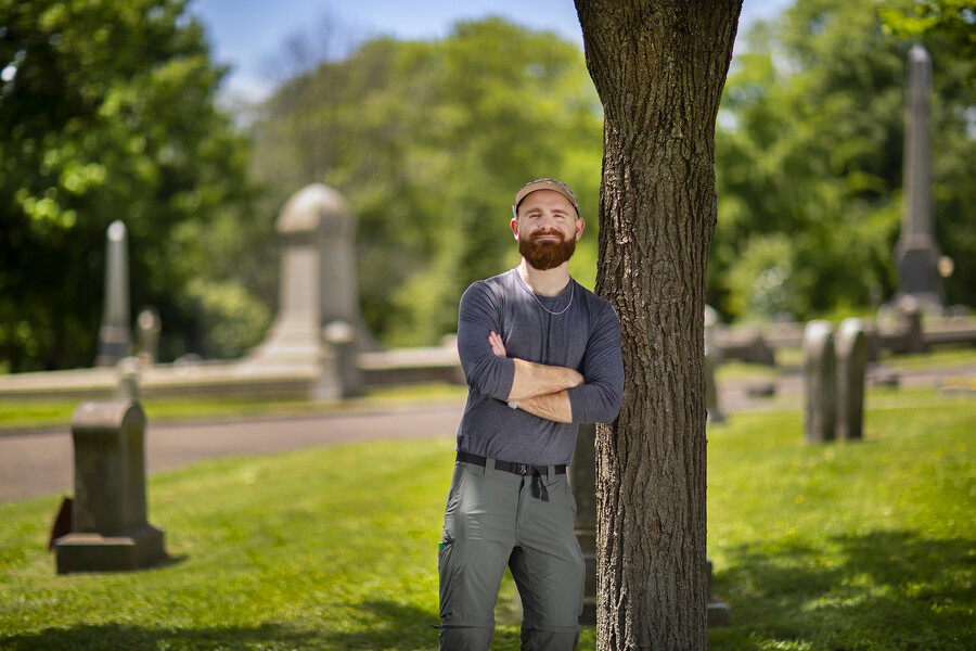 A person leans against a tree in a cemetery setting