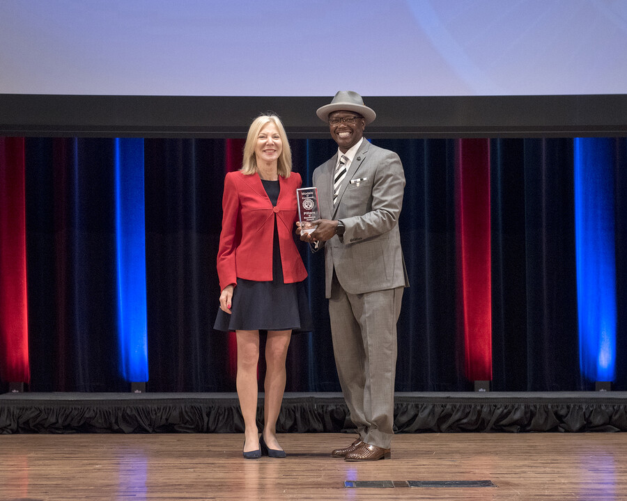 Amy Gutmann and Lorenzo Jackson on stage, Jackson holds an award.