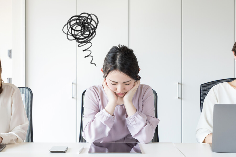 person seated at desk beside two other people with a scribble drawing representing dark thoughts above their head