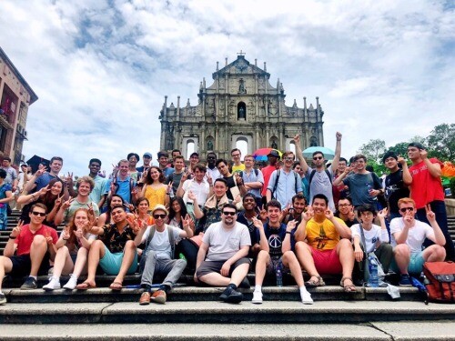 Many people sitting in front of a historic building. 
