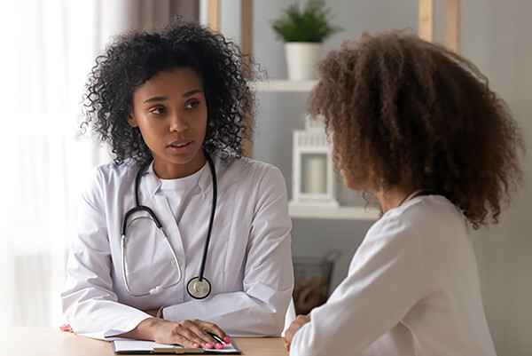 Doctor in white coat with stethoscope sitting by window talking to an adolescent