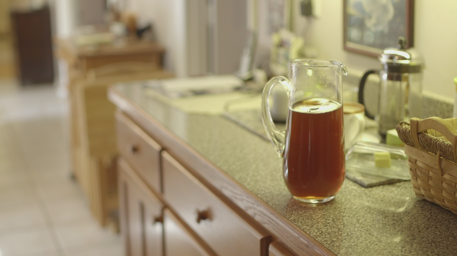 A glass pitcher filled with sweet tea on a laminate counter, with other kitchen items blurred in the background.