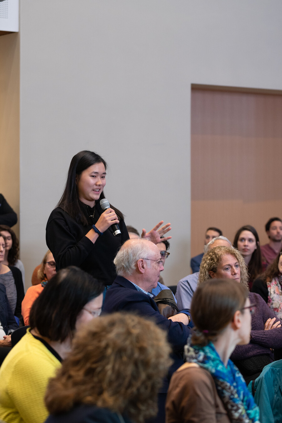 Student standing in audience speaking a question into a microphone.