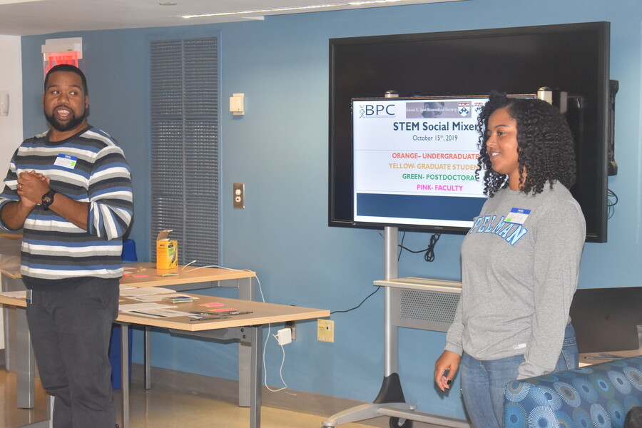 Two people stand on either side of a monitor with "STEM Social Mixer" on it