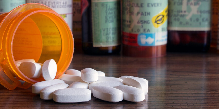 closeup of prescription pill container on its side with white oblong pills spilling out.