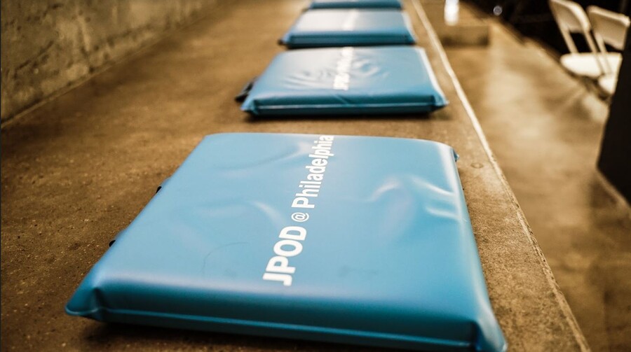 a line of blue chair cushions along a concrete bench, each reads JPOD @ Philadelphia
