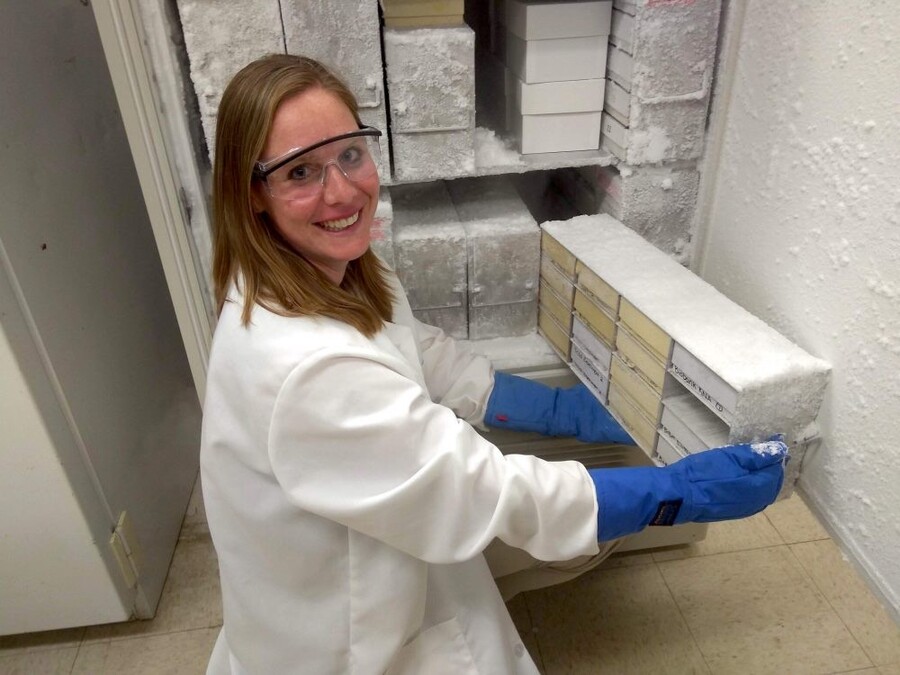 Veterinary scientist in lab coat, gloves and goggles smiles while handling frozen biological samples 