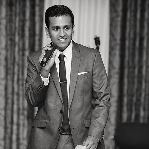 A person in a suit and tie holding a freestanding microphone. 