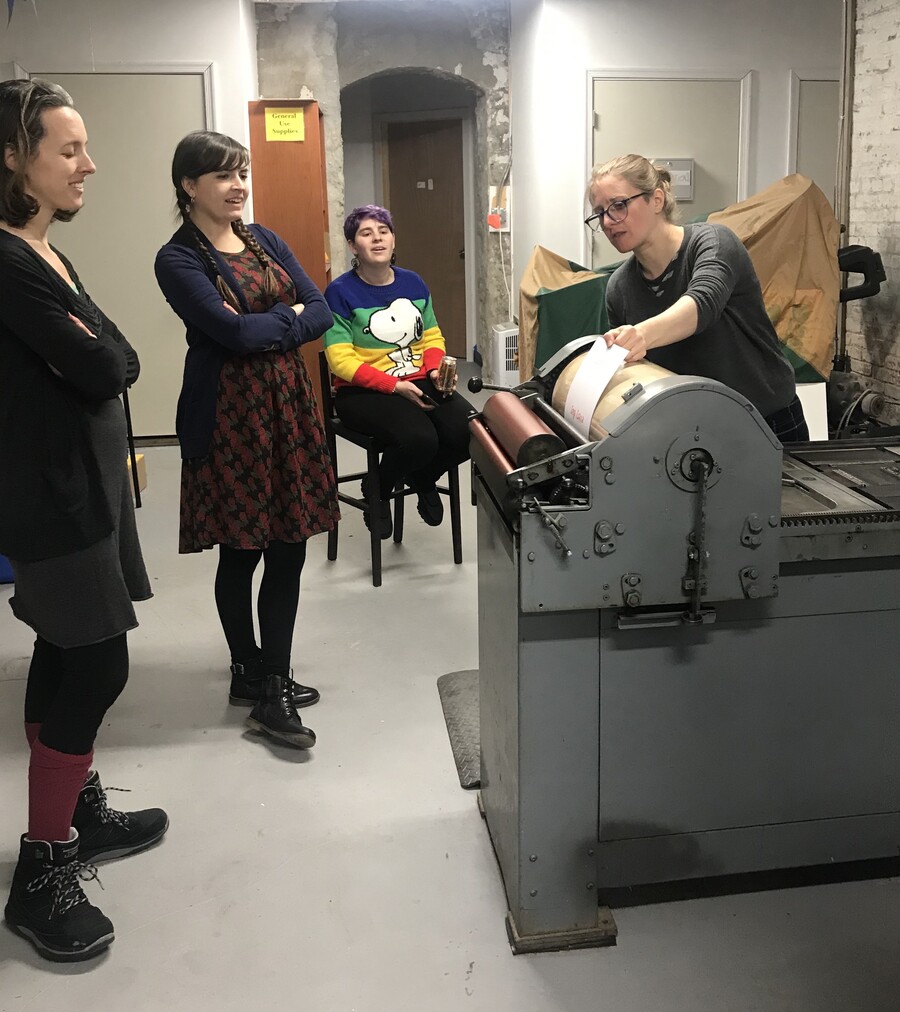 A person demonstrates the use of a letterpress machine while three others observe