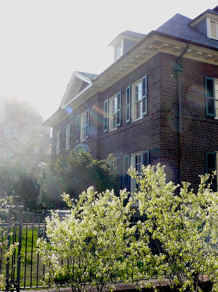 Brick building with shutters on windows and bushes in front