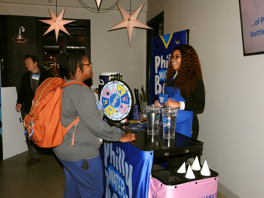 Person approaches another person in a booth with sign saying "Philly Water" at a celebratory event