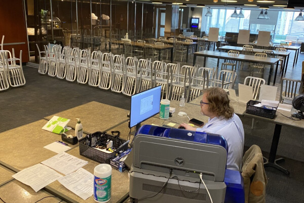 Person sitting at a computer in a room with empty tables and chairs stacked. 
