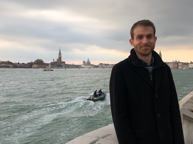 Person stands on a bridge with St. Mark's Basilica and Campanile in Venice, Italy, across the water in the background.